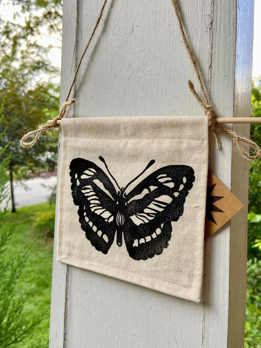 Decorative pendant with a black butterfly design hanging on a wooden post outdoors.