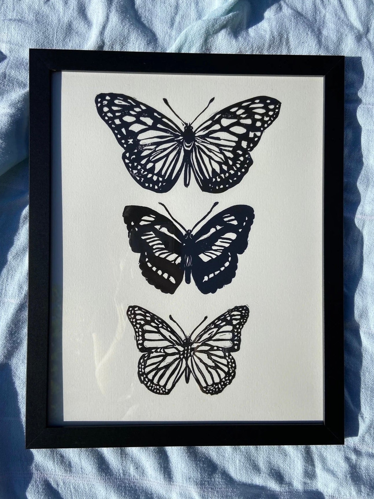 Framed artwork with black butterfly prints on a light blue fabric background