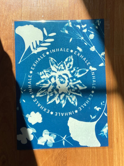 Blue cyanotype print with white floral design and the words "inhale exhale" on a wooden surface